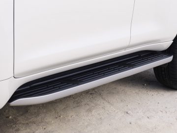 Close-up van een zijstap op een witte Toyota Land Cruiser, waarbij het ontwerp en de plaatsing tussen de voor- en achterwielen worden getoond.
