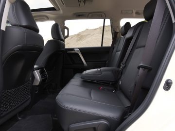 Binnenaanzicht van een Toyota Land Cruiser met lederen achterstoelen, open voordeur en landschap zichtbaar door ramen.