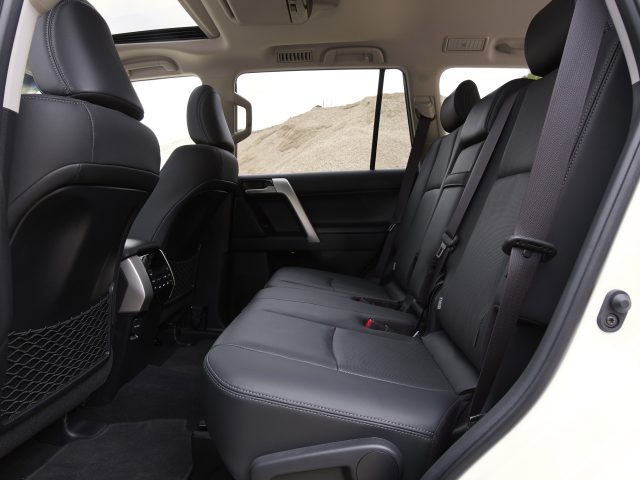 Binnenaanzicht van een Toyota Land Cruiser met de achterbank, de deur en een deel van het dashboard, met een zandduin zichtbaar door het raam.