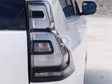 Close-up van het achterlicht en een deel van de zijkant van een witte Toyota Land Cruiser, geparkeerd met de deur open.