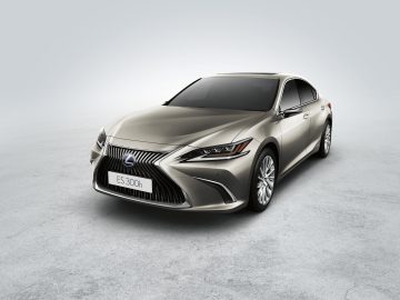 Een beige Lexus ES 300h sedan, schuin geplaatst op een effen grijze achtergrond.