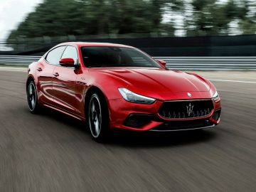 Een rode Maserati Ghibli die op snelheid racet op een racecircuit, wat zijn gestroomlijnde ontwerp en dynamische uitstraling benadrukt.