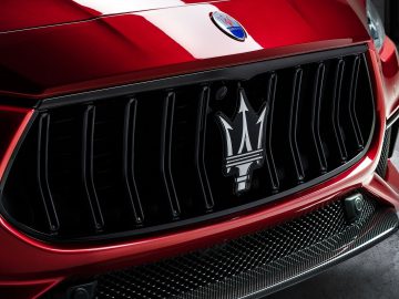 Close-up van de grille van een rode Maserati Ghibli met het iconische drietandlogo.