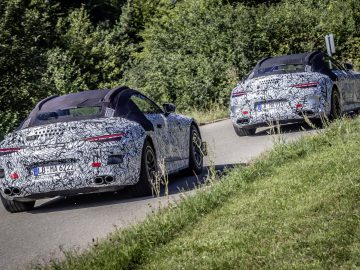 Twee gecamoufleerde Mercedes-Benz SL-sportwagens rijden op een zonnige weg en ondergaan waarschijnlijk tests.