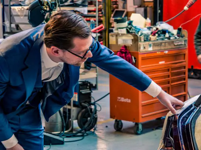 Een man in pak inspecteert Rolls-Royce Silver Spectre Shooting Brake-componenten in een industriële werkplaats.