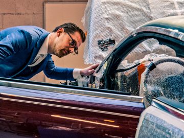 Man in pak inspecteert het interieur van een vintage Rolls-Royce Silver Spectre Shooting Brake, verpakt in beschermende noppenfolie.