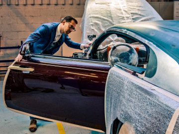Man in een werkplaats die de deur van een vintage Rolls-Royce minutieus restaureert, waarbij de auto gedeeltelijk bedekt is met een beschermfolie.