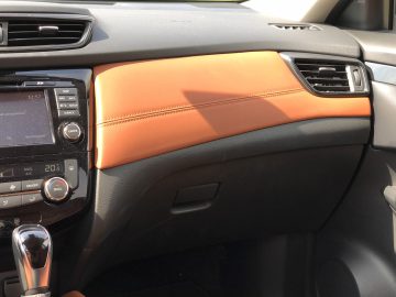 Interieur van een Nissan X-Trail met een dashboard met een oranje lederen paneel, digitale scherminterface en versnellingspook.