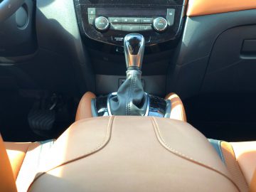 Binnenaanzicht van een Nissan X-Trail, waarbij de lederen stoelen, versnellingspook en dashboard bij daglicht worden benadrukt.