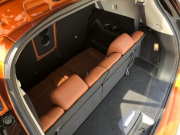 Achteraanzicht van een Nissan X-Trail met een open kofferbak met opgevouwen bruinleren stoelen en opbergvakken aan de binnenkant.