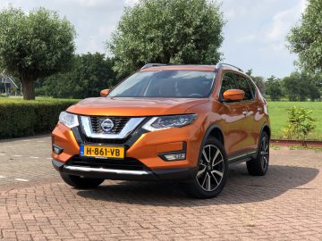 Nissan X-Trail geparkeerd op een verhard terrein met bomen en gras op de achtergrond op een zonnige dag.