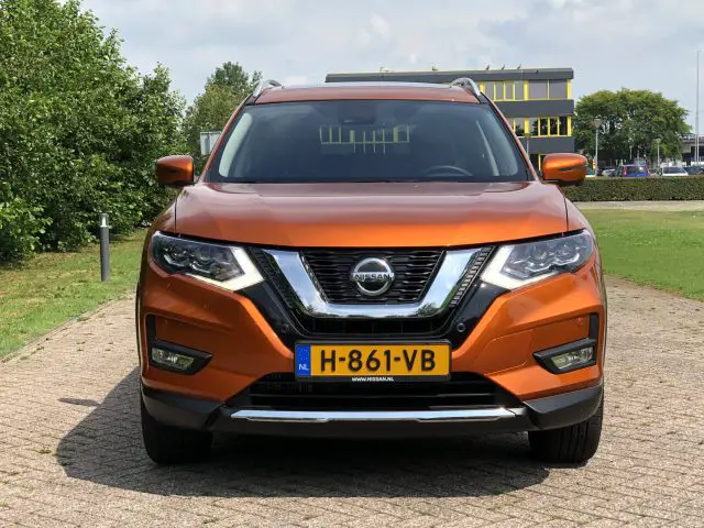 Een koperkleurige Nissan X-Trail geparkeerd voor een gebouw op een zonnige dag.