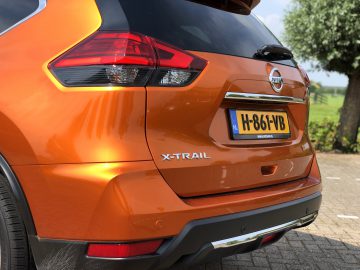 Close-up van de achterkant van een oranje Nissan X-Trail die buiten geparkeerd staat, met de nadruk op het achterlicht en de kentekenplaat.