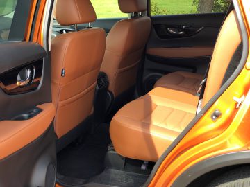 Binnenaanzicht van een Nissan X-Trail met oranje lederen achterbank en open deur.