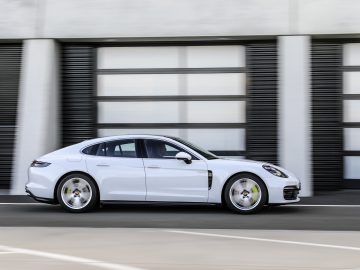 Een Porsche Panamera in beweging op een weg met een onscherpe achtergrond van horizontale lijnen op een gebouw.