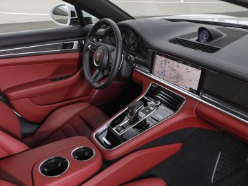 Binnenaanzicht van een Porsche Panamera met roodleren stoelen, een strak dashboard met digitale displays en een houten paneelafwerking.
