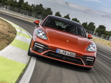 Een rode Porsche Panamera-sportwagen die over een racecircuit snelt en dynamisch kantelt als hij een bocht neemt.