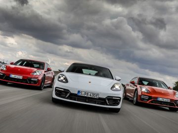 Drie Porsche Panamera-auto's in rood, wit en oranje, te hard rijdend op een bewolkte dag.