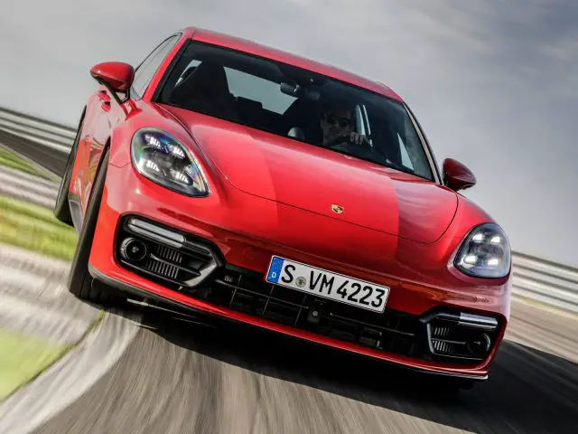 Rode Porsche Panamera sportwagen rijdt met hoge snelheid op een circuit, bestuurder zichtbaar door de voorruit.