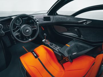 Interieur van een Gordon Murray Automotive T.50-sportwagen met feloranje stoelen, een handmatige versnellingspook en een dashboard met digitale displays.