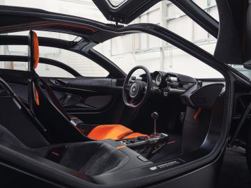 Interieur van een Gordon Murray Automotive T.50 sportwagen met bestuurdersstoel, stuur en dashboard met zwarte en oranje bekleding.