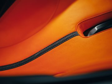 Close-up van een oranje Gordon Murray Automotive T.50 autostoeltje met zwart stiksel.