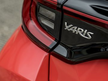 Close-up van een rode Toyota Yaris, waarbij de nadruk ligt op het naamplaatje van het model en een deel van het achterlicht op de kofferbak van de auto.
