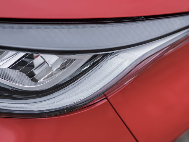 Close-up van de koplamp van een moderne Toyota Yaris op een rood voertuig, met de nadruk op het gedetailleerde ontwerp en de heldere lens.