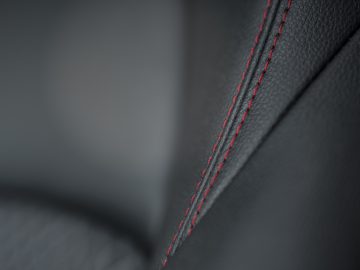 Close-up van een zwart lederen Toyota Yaris autostoeltje met rode stiksels.