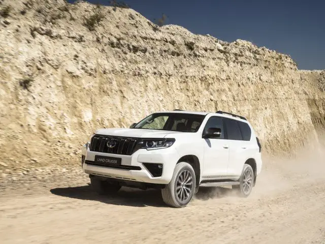 Een Toyota Land Cruiser die over een stoffige woestijnweg rijdt, waarbij rotsen en zand een dynamische achtergrond creëren.