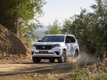 Een Toyota Land Cruiser die over een stoffig pad door beboste heuvels rijdt.