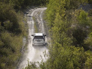 Een witte Toyota Land Cruiser die over een bochtige onverharde weg door een dicht groen bos rijdt.