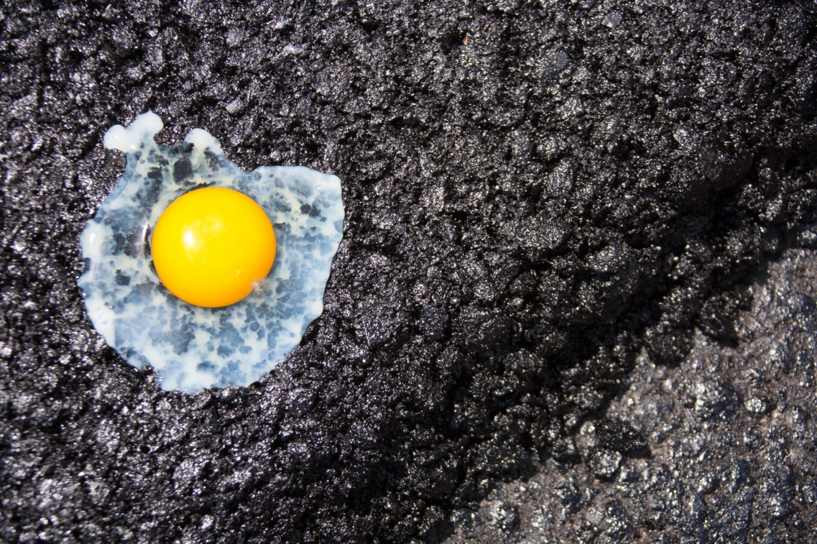 Een ei met de zonnige kant naar boven op een donkere, getextureerde winterband, waarbij de felgele dooier en het doorschijnende eiwit worden benadrukt.
