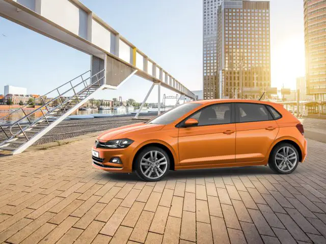 Orange autoverkoop juli 2020 auto geparkeerd op een stenen stoep bij een rivier met moderne gebouwen en een brug op de achtergrond tijdens zonsondergang.