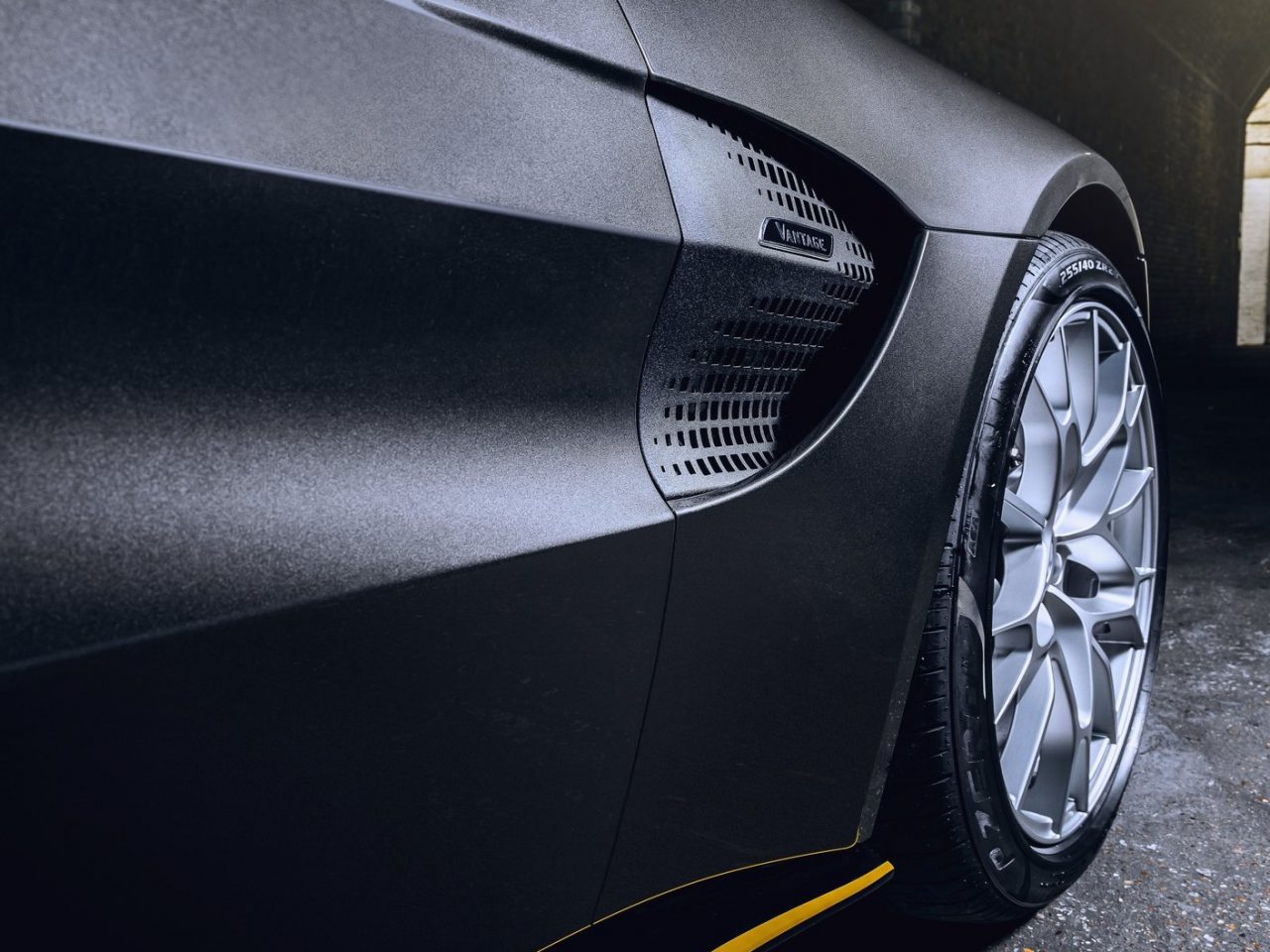 Close-up van het achterwiel en de ventilatieopeningen aan de zijkant van een zwarte droomauto, waarbij het strakke ontwerp en ingewikkelde wielpatroon benadrukt worden.