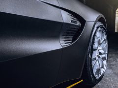 Close-up van het achterwiel en de ventilatieopeningen aan de zijkant van een zwarte droomauto, waarbij het strakke ontwerp en ingewikkelde wielpatroon benadrukt worden.