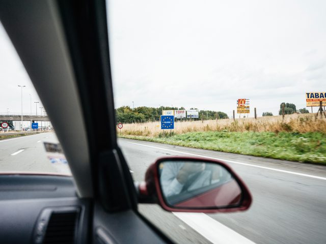Uitzicht vanuit een auto met een snelweg met verkeersborden en weelderig groen in Nederland, zijspiegel zichtbaar op de voorgrond.