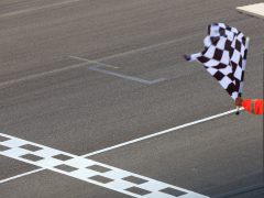 Een persoon in een oranje mouw die met een geblokte vlag zwaait bij de finish van een miniatuurracebaan.