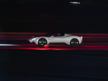 Een zilveren Maserati MC20 die 's nachts te hard rijdt met bewegingsonscherpte die de snelheid benadrukt, tegen een donkere achtergrond.