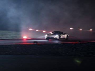 Maserati MC20-sportwagen die 's nachts over een racecircuit rijdt met intense bandenrook en slecht verlichte rode baanverlichting.