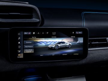 Auto-infotainmentscherm met Maserati MC20-bedieningselementen en -instellingen met een geanimeerde auto op de achtergrond van een racecircuit.