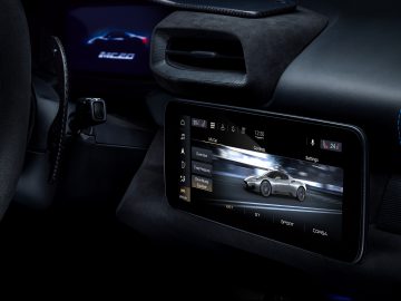 Binnenaanzicht van een Maserati MC20 met een digitaal dashboarddisplay met voertuiginstellingen op het scherm, gemarkeerd door blauwe omgevingsverlichting.
