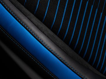 Close-up van een Maserati MC20-autostoeltje met zwart leer en blauwe stof met een gestreept patroon.