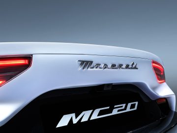 Achteraanzicht van een witte Maserati MC20, met de nadruk op het logo en het achterlicht, tegen een grijze achtergrond.