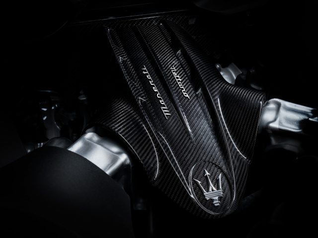 Close-up van de motorkap van een Maserati MC20-auto van koolstofvezel, met het logo van het merk en het ingewikkelde weefpatroon.