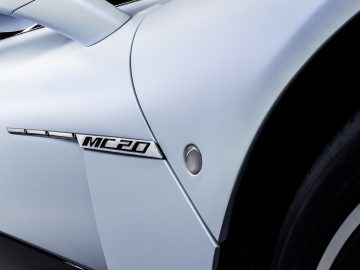 Close-up van een witte Maserati MC20 met de modelnaam 'MC20' op de zijkant, met de nadruk op het strakke ontwerp en de band.
