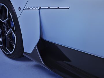 Close-up van een blauwe Maserati MC20-sportwagen, met de nadruk op het achterwiel en het zijpaneel met het 'MC20'-logo, wat het strakke ontwerp en de koolstofvezeldetails benadrukt.