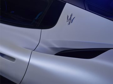 Close-up van een zilveren autodeur met een Maserati MC20-embleem, wat het strakke ontwerp en het gladde oppervlak benadrukt.