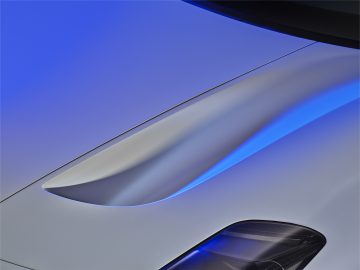 Close-up van de slanke, metallic zilveren carrosserie van een Maserati MC20, met blauw omgevingslicht dat reflecteert op het gebogen oppervlak.