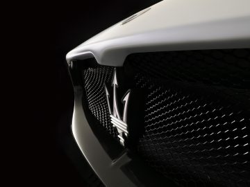 Close-up van de grille en het embleem van een Maserati MC20, verlicht onder dramatische verlichting tegen een donkere achtergrond.